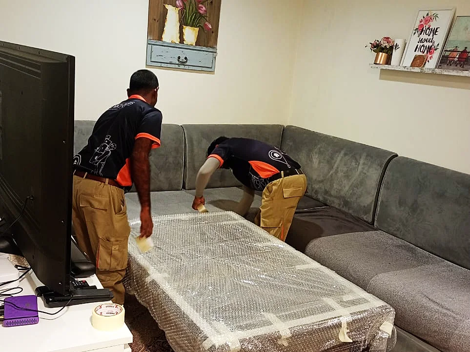 GI Movers crew wrapping a coffee table in an Abu Dhabi apartment