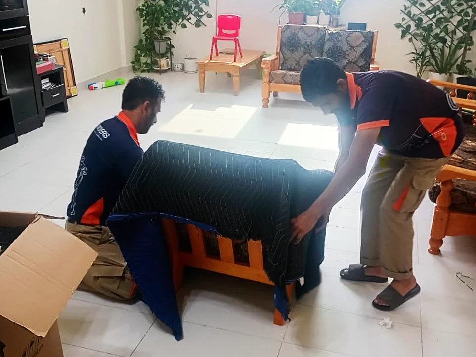 GI Movers crew wrapping a sofa in moving blankets before storage in Dubai